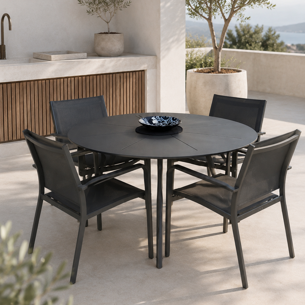 Outdoor dining set with round table and chairs on a patio with a view of the sea.